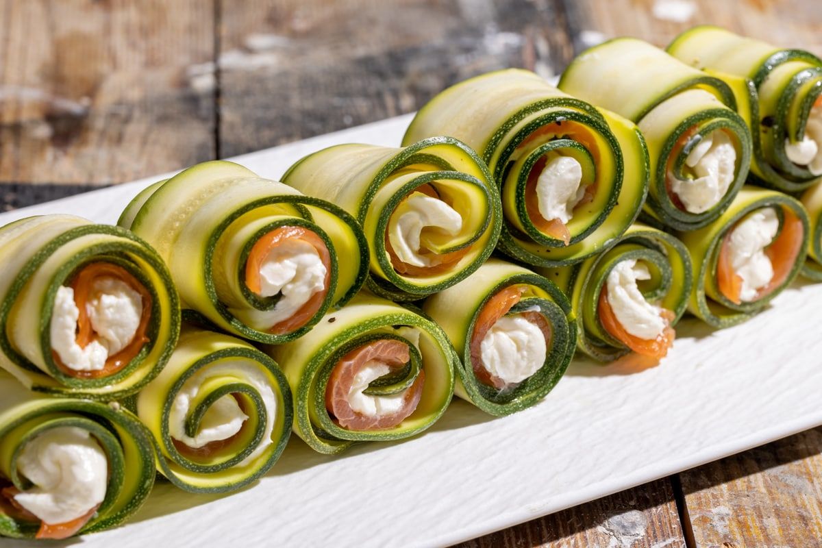 Ich rolle die Zucchinischeiben mit Käse und Schinken auf. Auf dem Tisch sehen die Röllchen luxuriös aus und sind innerhalb einer Minute verschwunden.