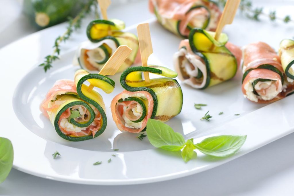 Ich rolle die Zucchinischeiben mit Käse und Schinken auf. Auf dem Tisch sehen die Röllchen luxuriös aus und sind innerhalb einer Minute verschwunden.