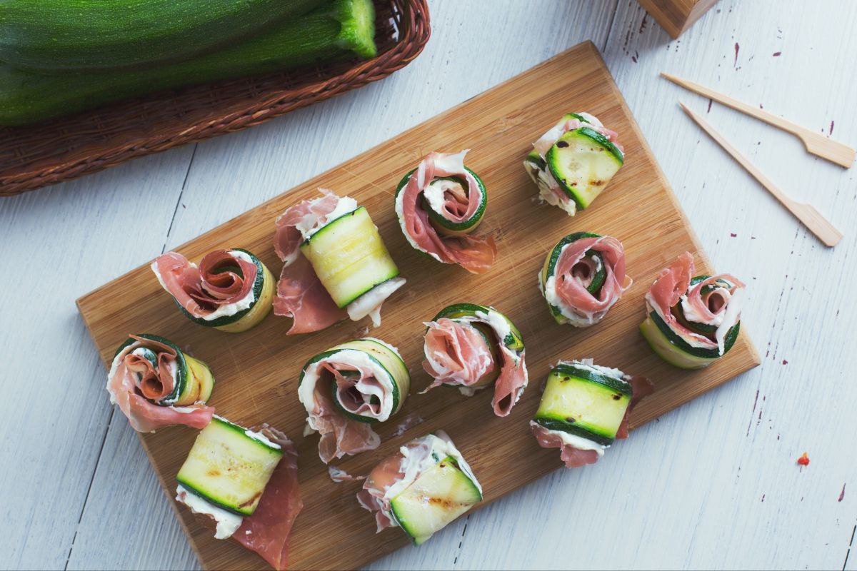 Ich rolle die Zucchinischeiben mit Käse und Schinken auf. Auf dem Tisch sehen die Röllchen luxuriös aus und sind innerhalb einer Minute verschwunden.